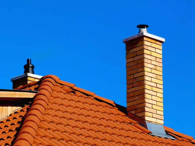 Brick chimney with a cowl above an orange tiled roof