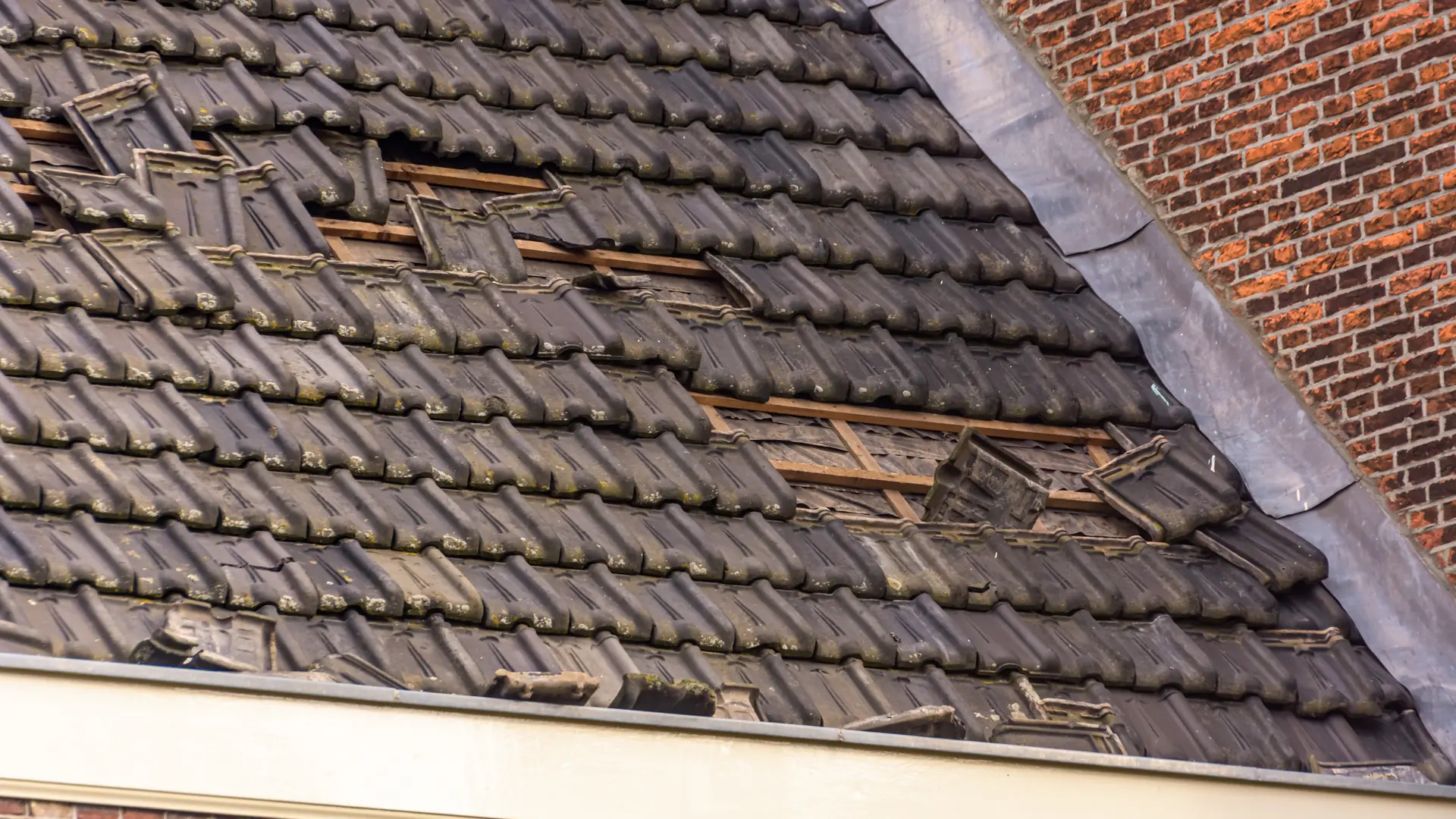 Tiled roof with tiles torn away beside a brick gable