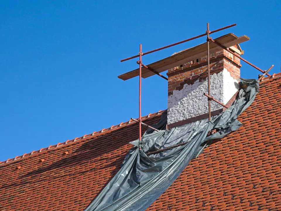 Protective sheeting and scaffold around a chimney on a red tiled roof