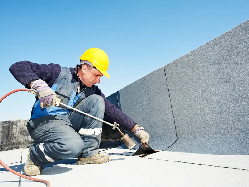 Roofer sealing a flat roof covering against a wall upstand